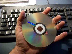 Picture of a DVD held in an adult-sized hand with a keyboard in the background.