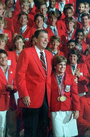 Picture of happy smiling people wearing red coats; in the front is President Reagan with arm around a short woman.